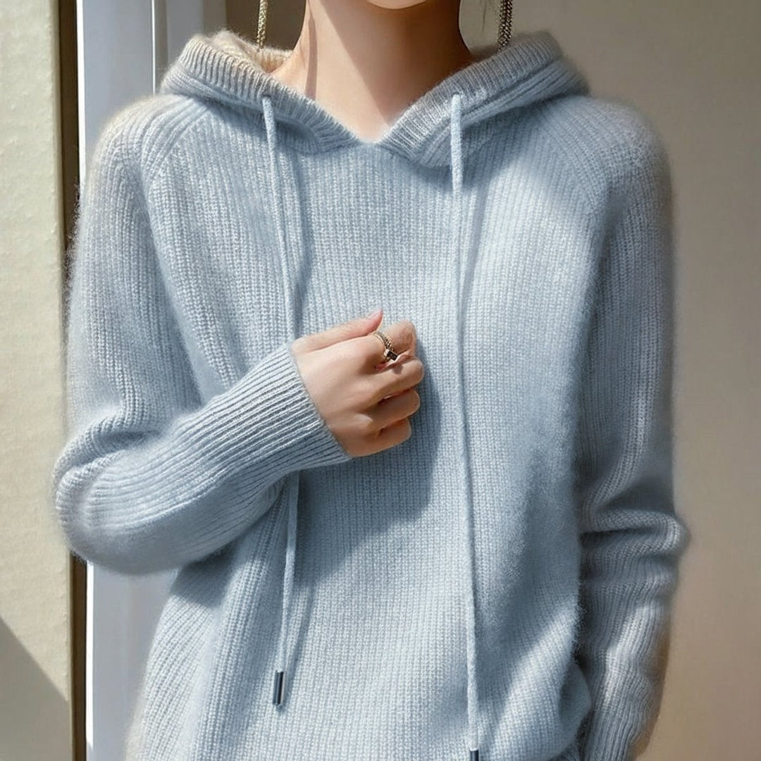 Vrouw in een lichtblauwe gebreide hoodie met koord en raglanmouwen, hand voor de borst | Boutique Moda