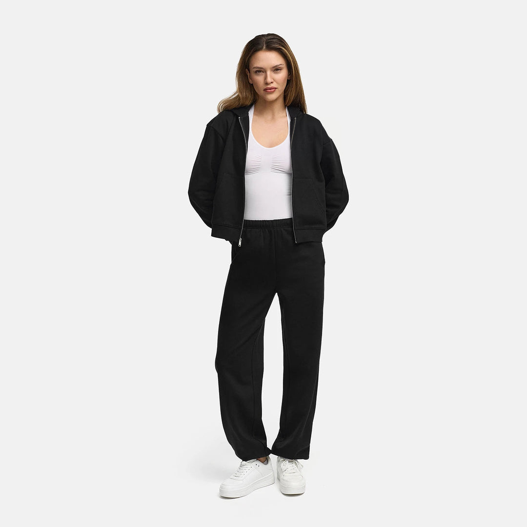 Vrouw draagt een zwart capuchonvest open over een wit topje met een bijpassende broek, ten voeten uit | Boutique Moda