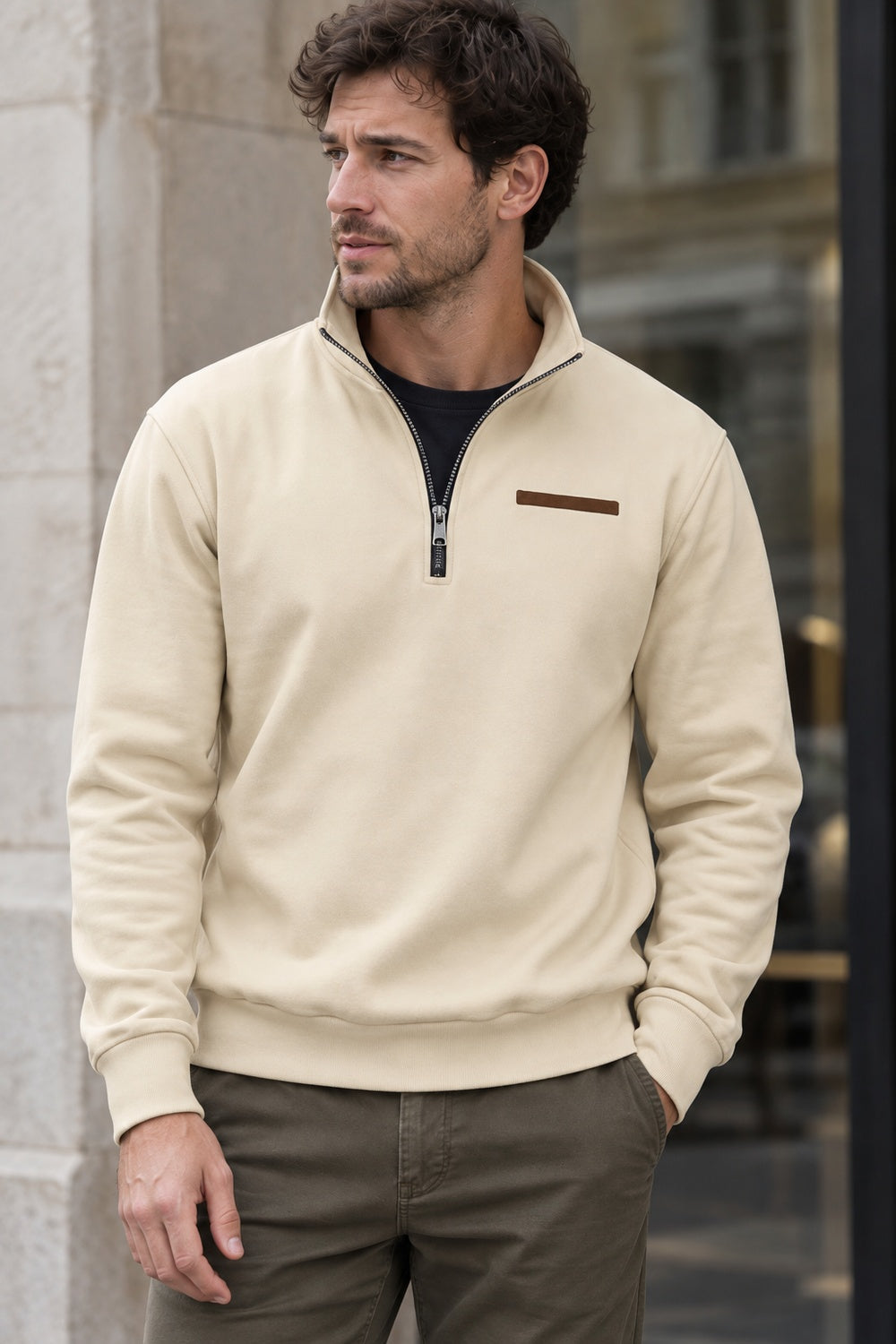 Man in een beige sweater met opstaande kraag over een zwart T-shirt, met een hand in zijn broekzak | Boutique Moda