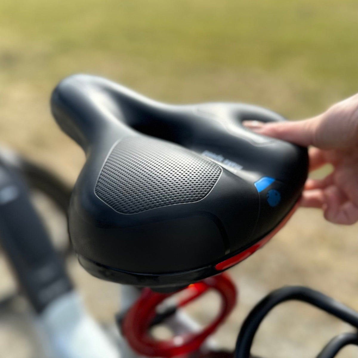 Zwart fietszadel met geperforeerd oppervlak, gemonteerd op fiets, hand raakt aan | Boutique Moda