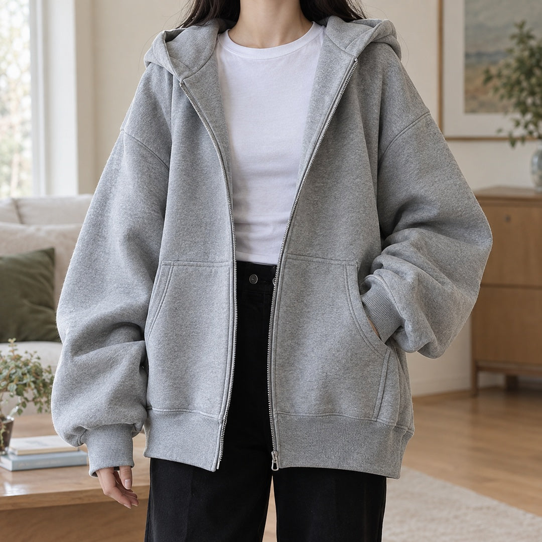 Vrouw draagt open grijs oversized capuchonvest over een wit T-shirt en een zwarte broek | Boutique Moda