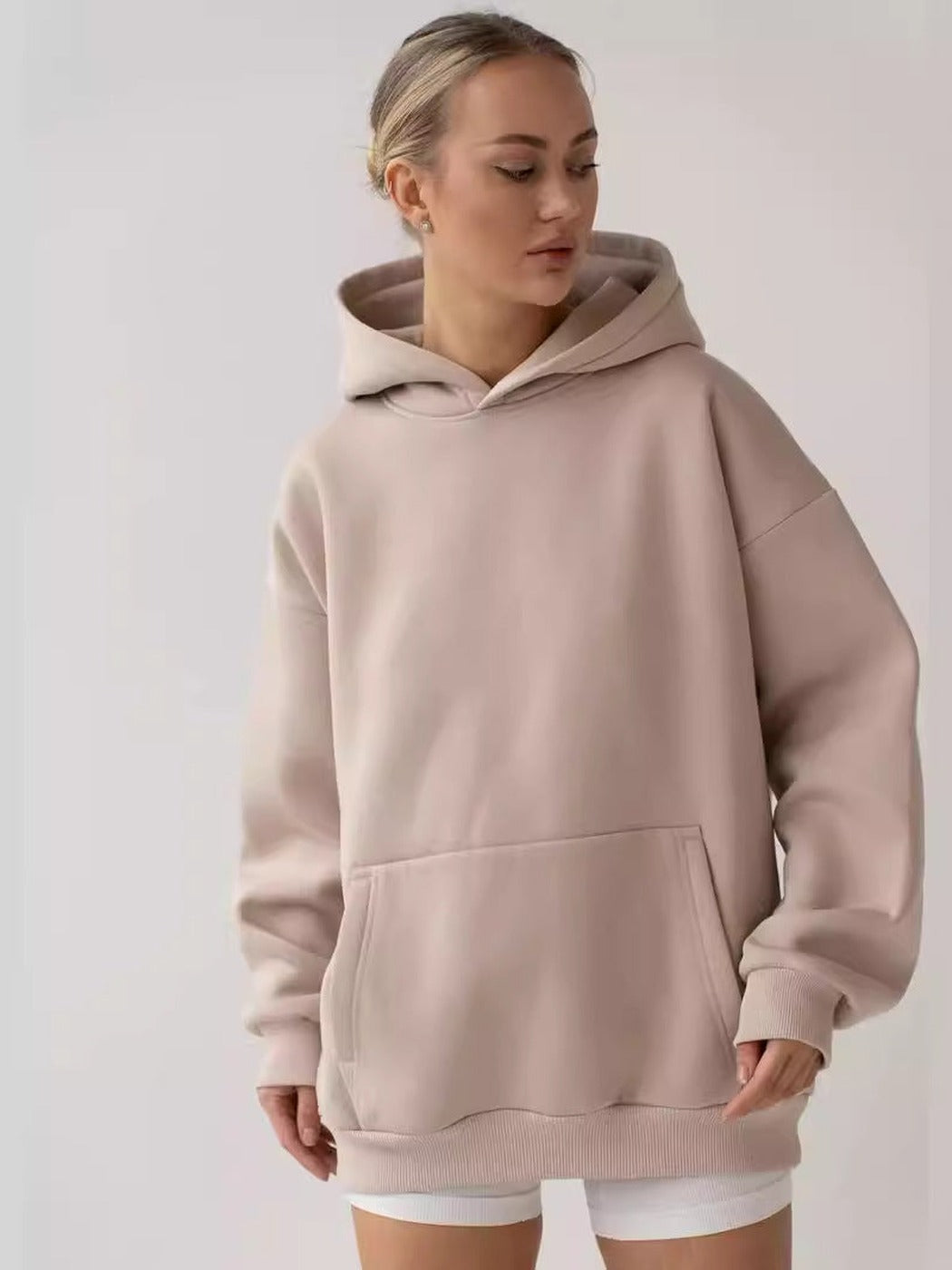 Vrouw in een taupe oversized hoodie met kangoeroezak en witte shorts | Boutique Moda