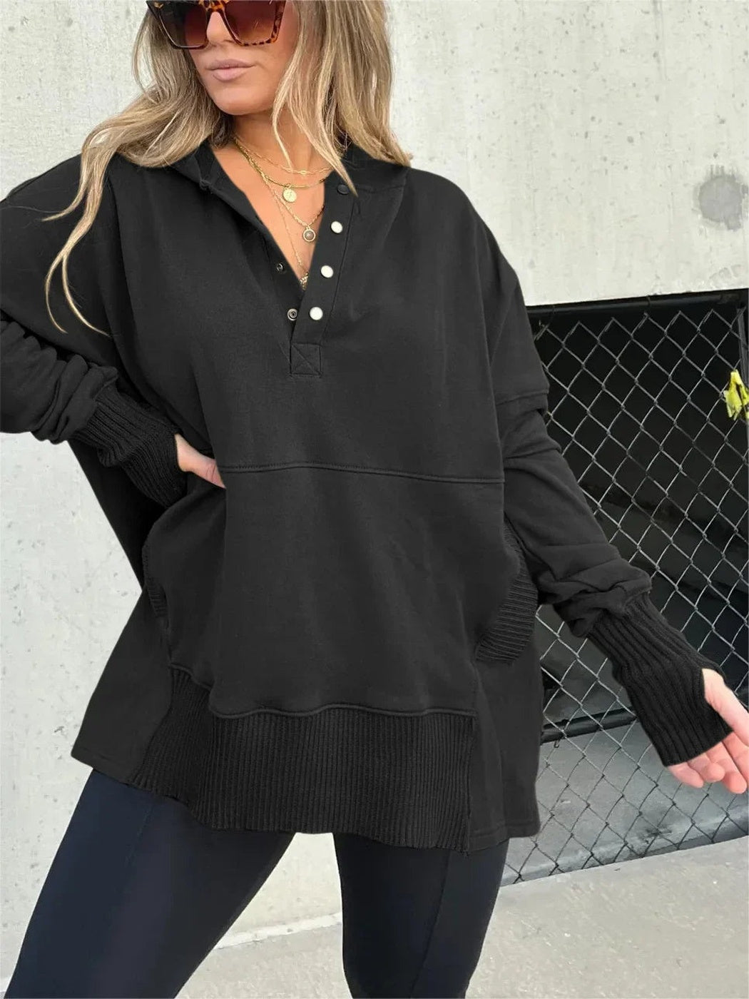 Vrouw in zwarte oversized trui met capuchon en knoopsluiting, hand op de heup | Boutique Moda