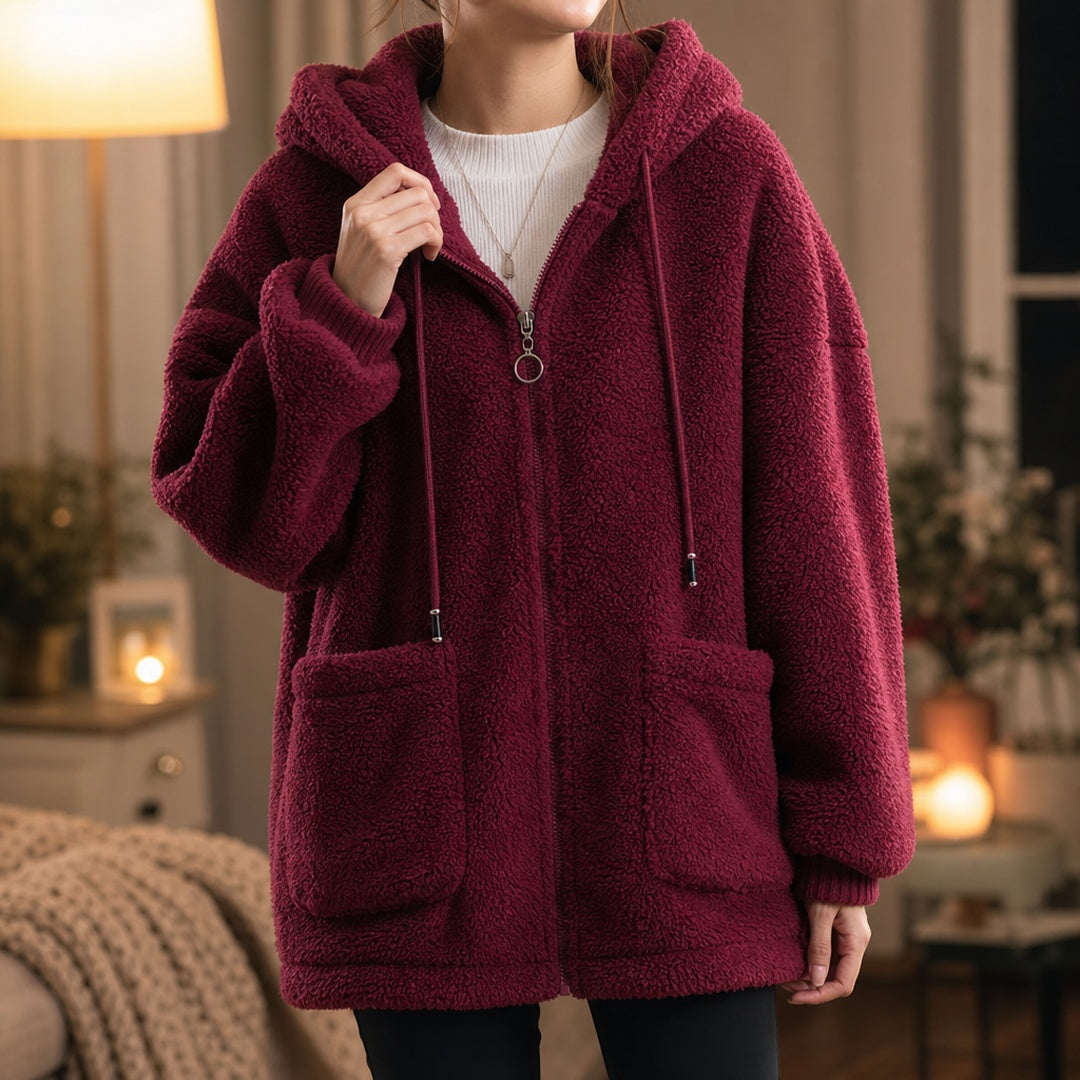 Vrouw in een bordeauxrood teddyvest met capuchon en ringvormige ritstrekker, met een hand aan de rand van de capuchon | Boutique Moda