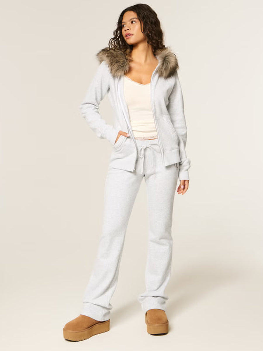 Vrouw in een open lichtgrijze hoodie met nepbont aan de capuchon, over een crèmekleurige top, hand in de zak | Boutique Moda