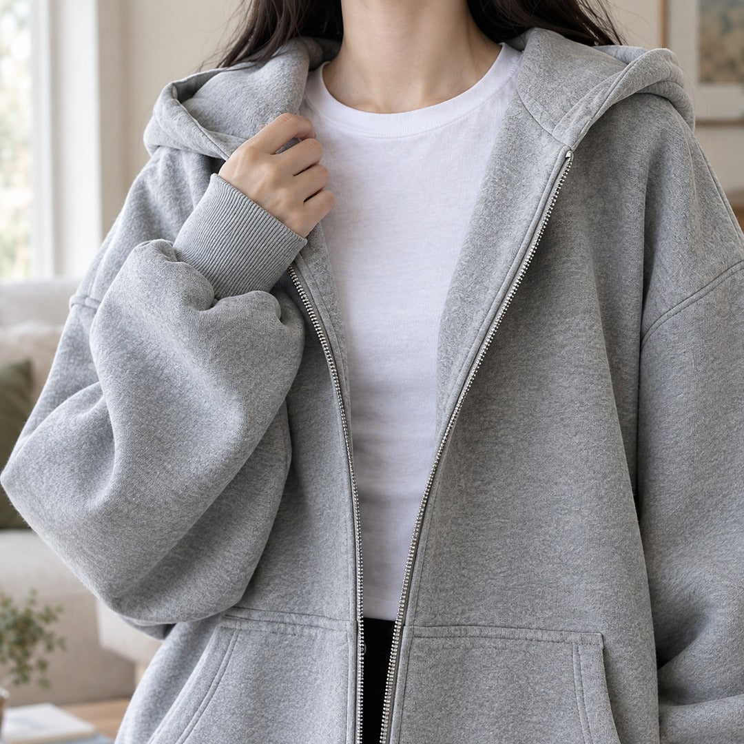 Close-up van het grijze capuchonvest: capuchon, rits en geribde boord, hand bij de rits | Boutique Moda