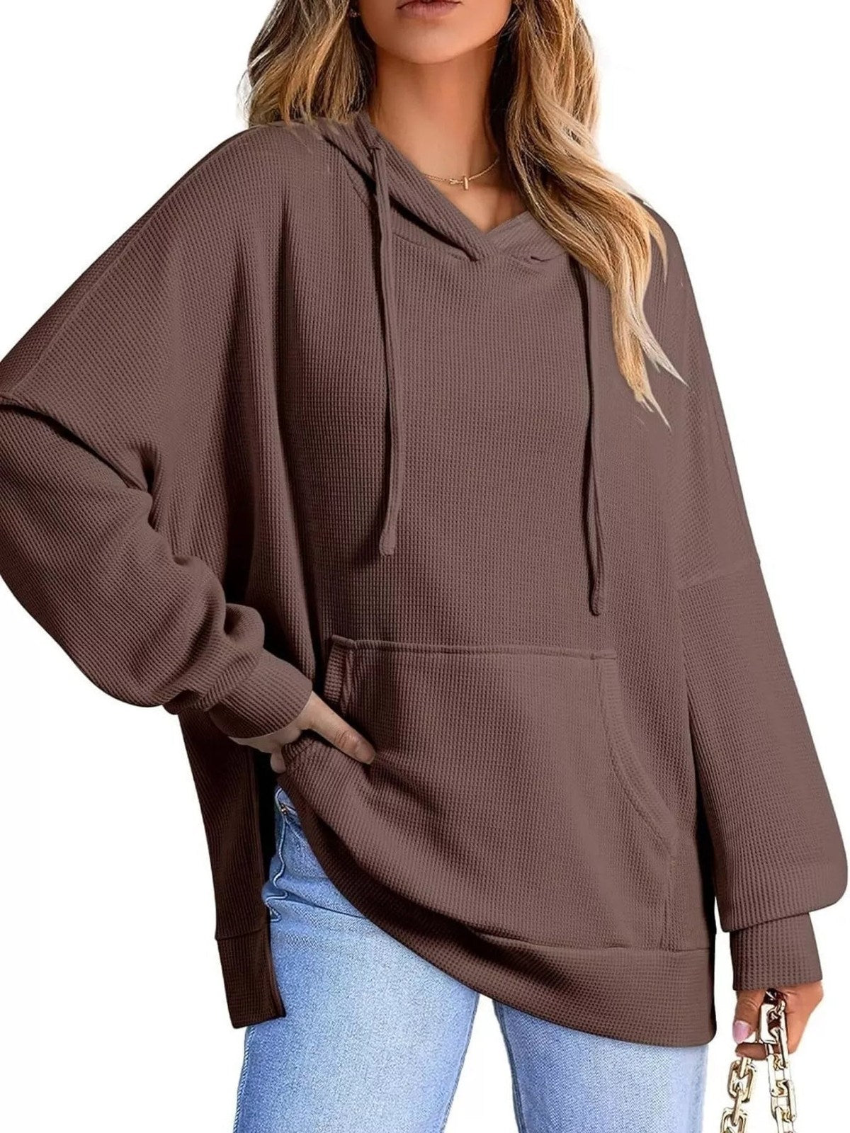 Vrouw in bruine oversized capuchontrui met kangoeroezak en zijsplitten | Boutique Moda
