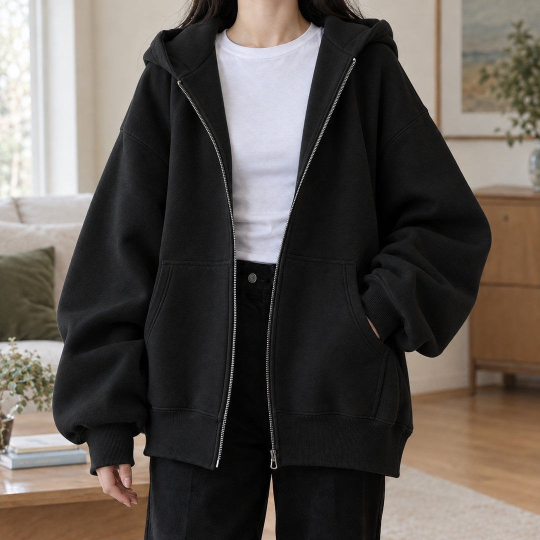 Vrouw draagt open zwart oversized capuchonvest over een wit T-shirt, hand in de zak | Boutique Moda
