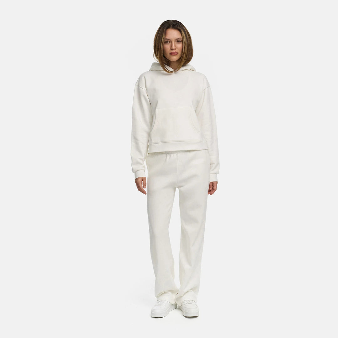Vrouw in een gebroken witte sweater met een bijpassende broek en witte sneakers, ten voeten uit | Boutique Moda