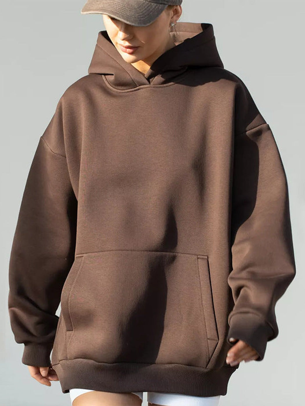 Vrouw met een grijze pet in een koffiebruine hoodie, blik naar beneden | Boutique Moda