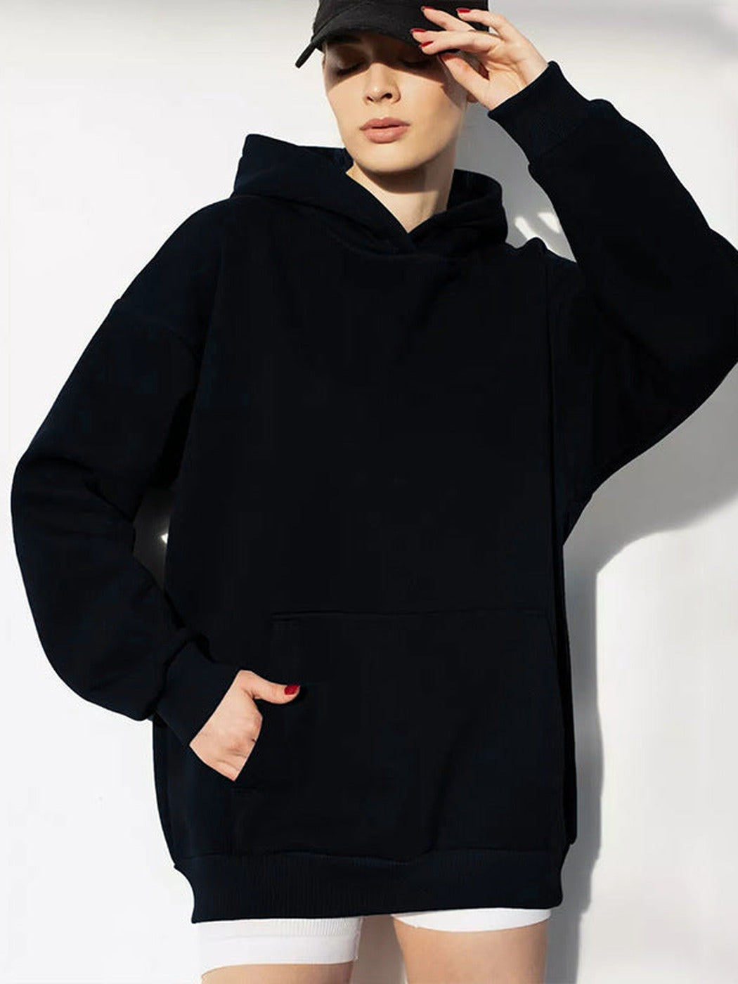 Vrouw met een zwarte pet in een zwarte hoodie, hand in de zak | Boutique Moda