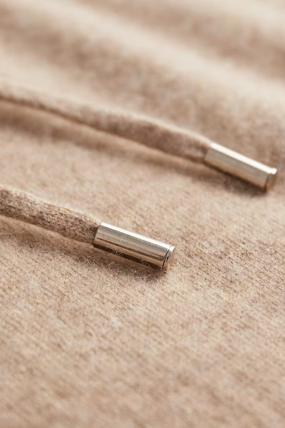 Gebreide trui met capuchon voor heren in beige, close-up van de metalen uiteinden van het koord