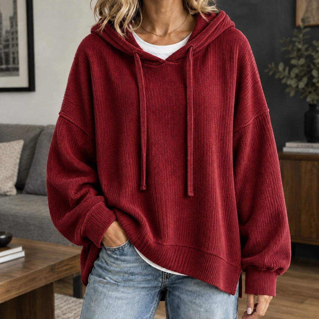 Vrouw in een wijnrode gebreide trui met koorden en brede ribboorden in de woonkamer | Boutique Moda