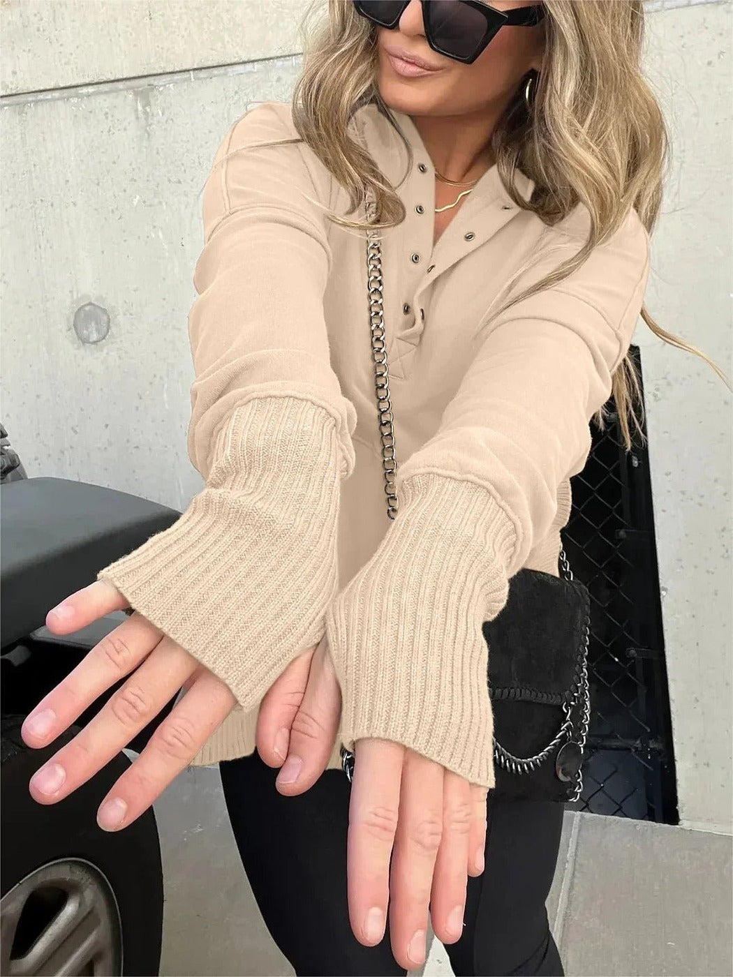 Beige trui met knoopsluiting en extra lange ribboorden, armen naar voren gestrekt | Boutique Moda