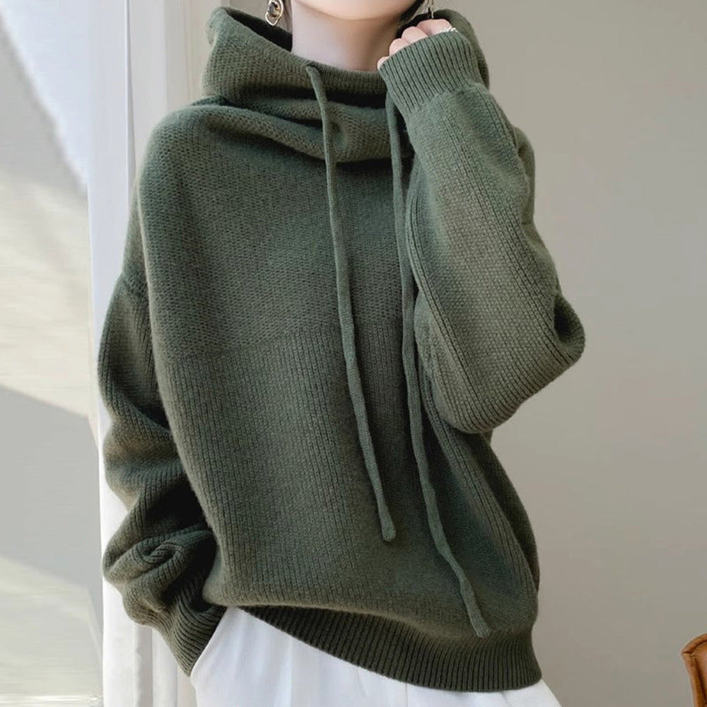 Vrouw in een dennengroene gebreide trui met een witte broek, hand bij de kraag | Boutique Moda