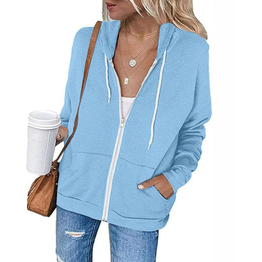 Vrouw in een lichtblauw vest met capuchon en zoomband, met een beker in de hand | Boutique Moda