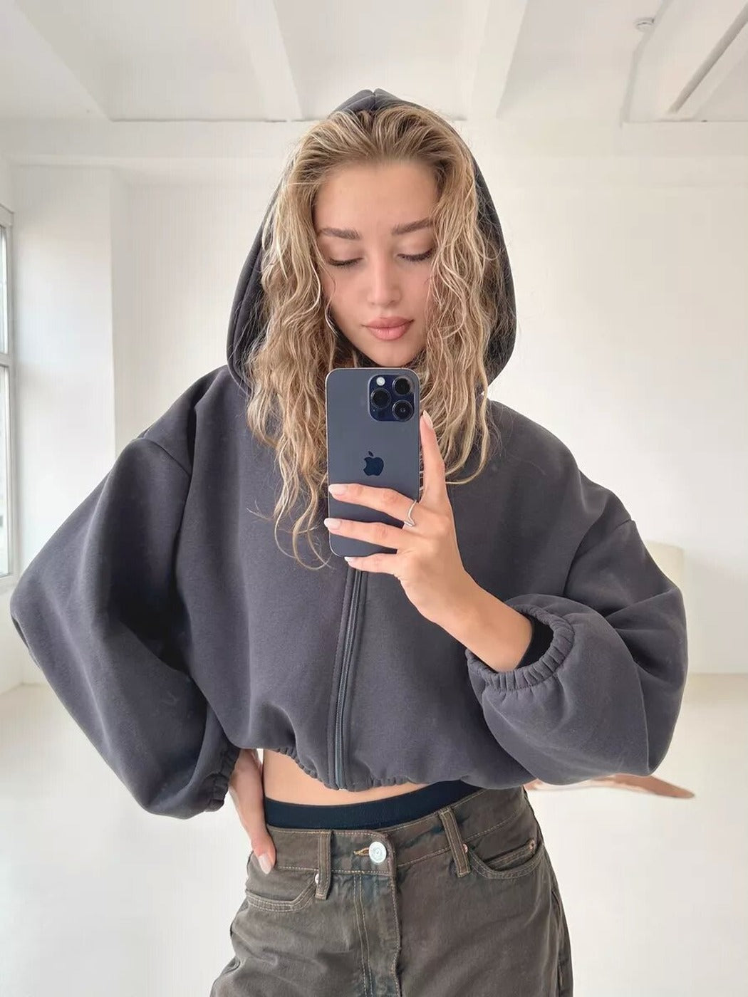 Vrouw in een donkergrijs oversized vest met capuchon in een lichte ruimte | Boutique Moda