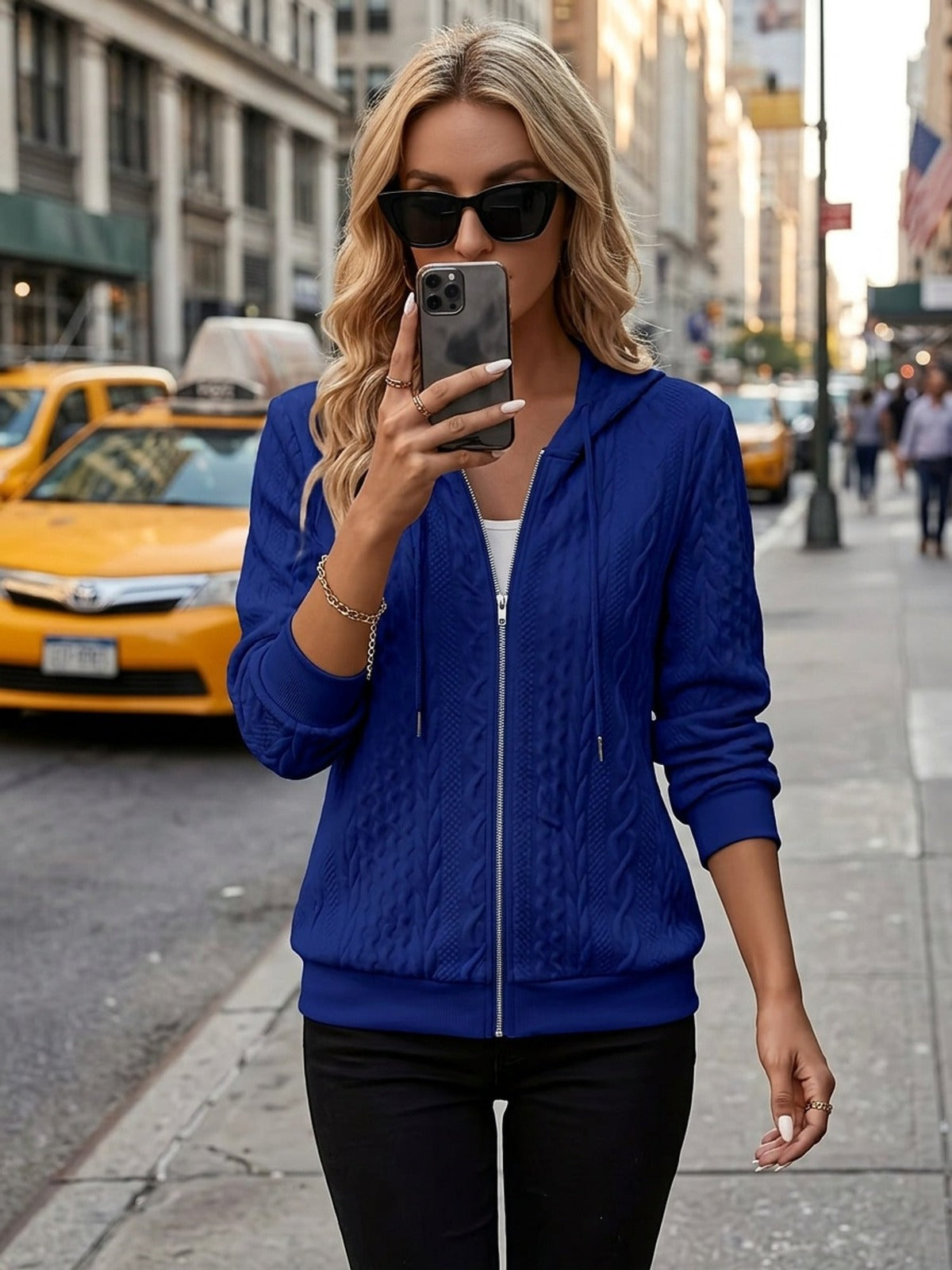 Vrouw draagt koningsblauwe hoodie met zonnebril en telefoon in een stadsstraat | Boutique Moda