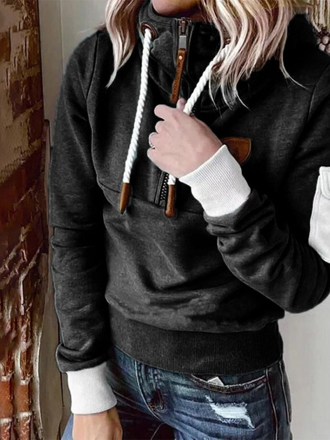 Vrouw in een zwarte hoodie die een koord vasthoudt, met een witte geribde boord aan de mouw | Boutique Moda