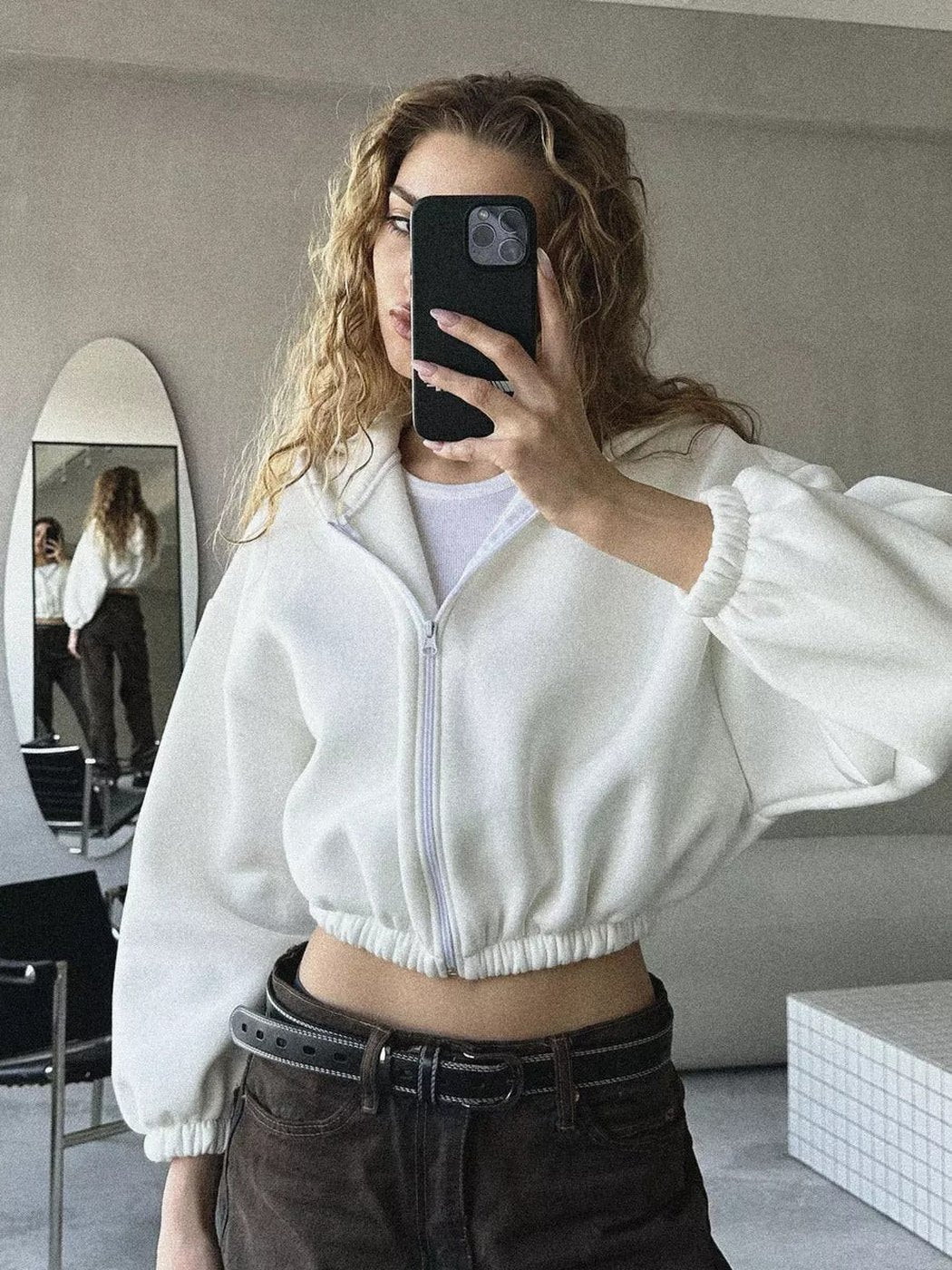 Vrouw in een wit kort vest over een wit topje, met een bruine jeans en riem | Boutique Moda