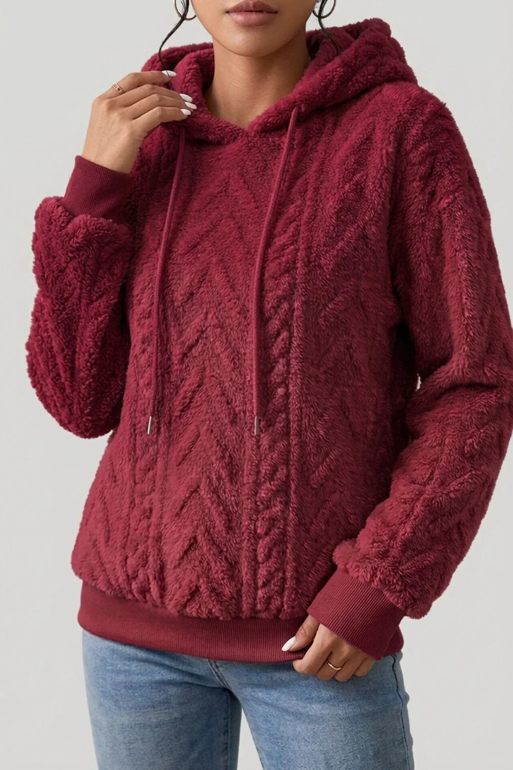 Vrouw in een bordeauxrode teddytrui met metalen uiteinden aan de koorden | Boutique Moda