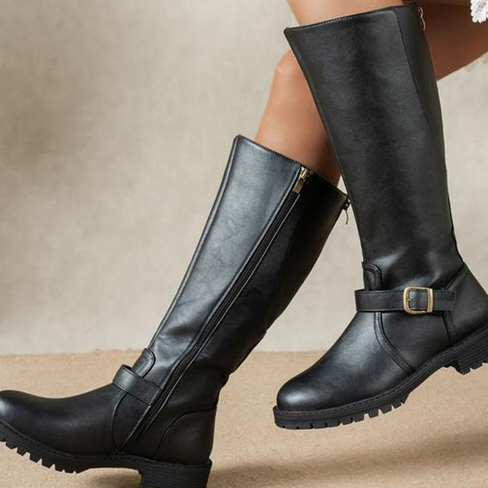 Zwarte hoge laarzen met gesp, gedragen door een persoon, close-up zijaanzicht | Boutique Moda