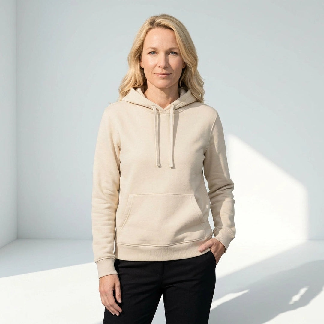 Vrouw draagt beige hoodie met kangoeroezak voor een lichte muur | Boutique Moda
