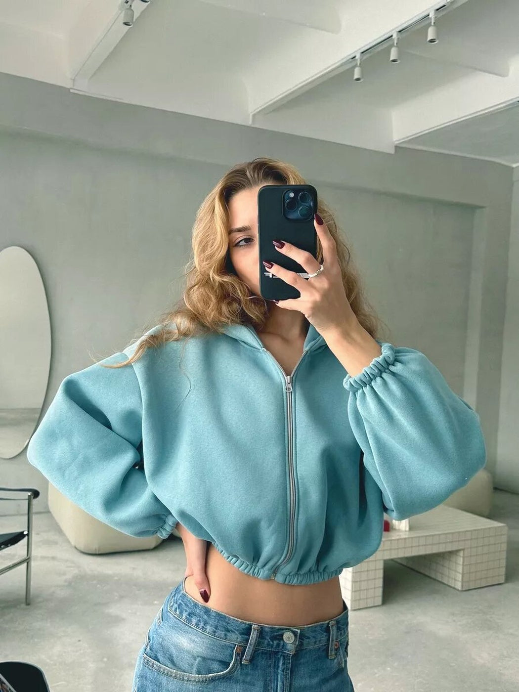 Vrouw in een turquoise kort vest met elastische boorden, hand op de taille | Boutique Moda