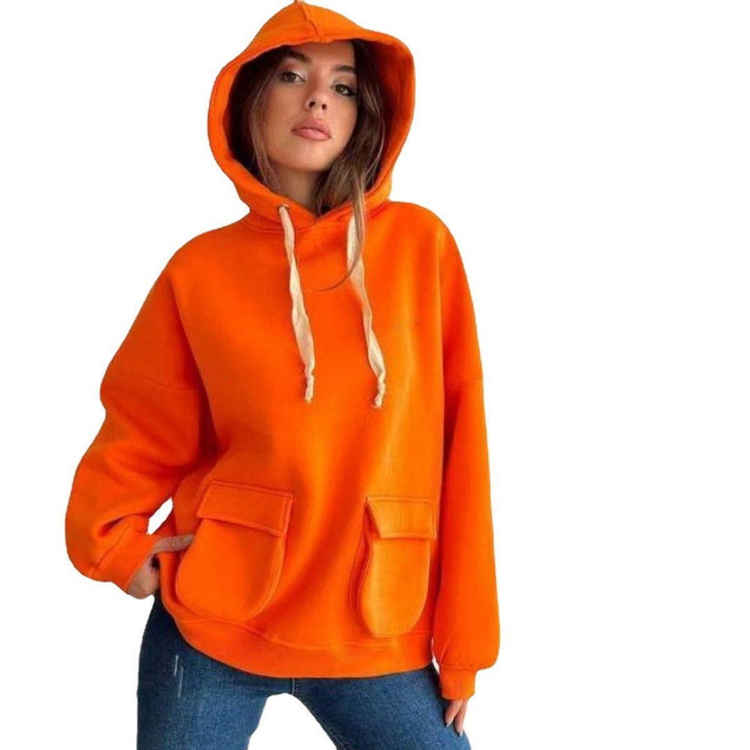 Vrouw in een oranje oversized hoodie met de capuchon op en een jeans | Boutique Moda
