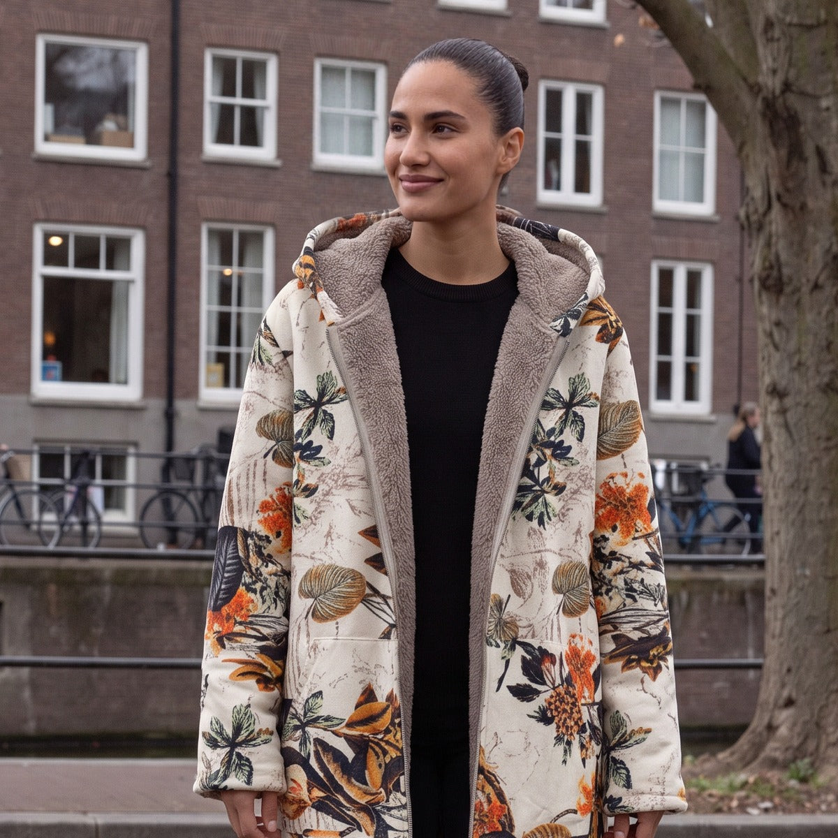 Omkeerbare winterjas met capuchon in crème met oranje bloemen, gedragen aan een Amsterdamse gracht