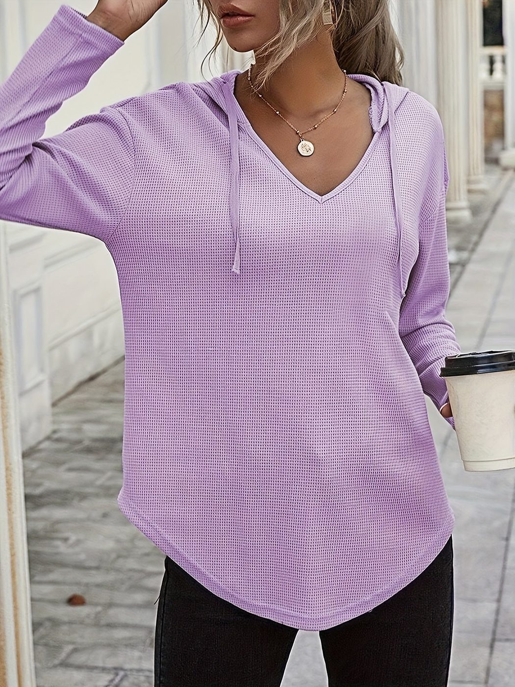 Vrouw in een lila hoodie met dun koord in een lichte straat, hand in het haar | Boutique Moda