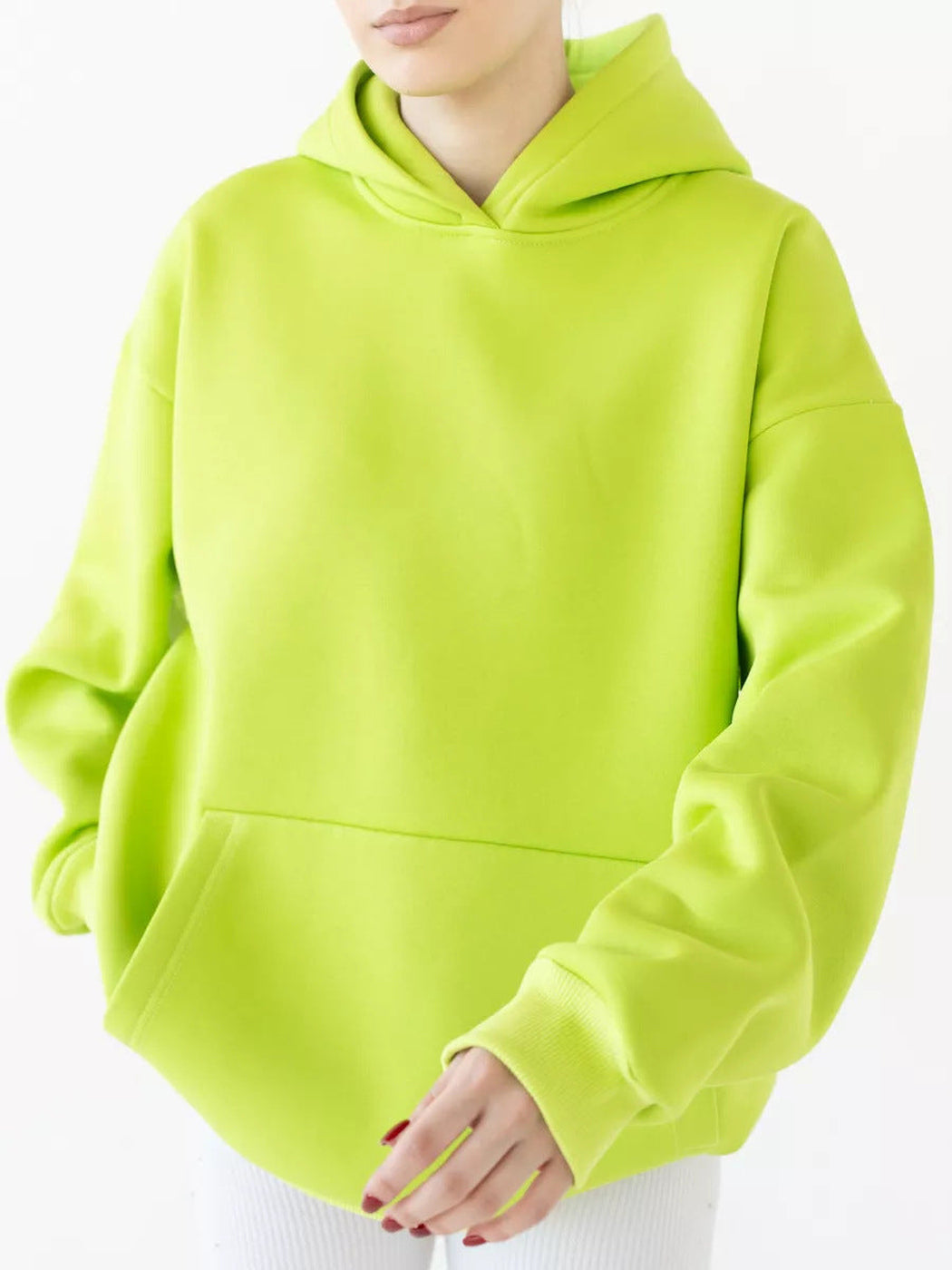 Vrouw in een limoengroene hoodie met ruime pasvorm, handen voor het lichaam | Boutique Moda