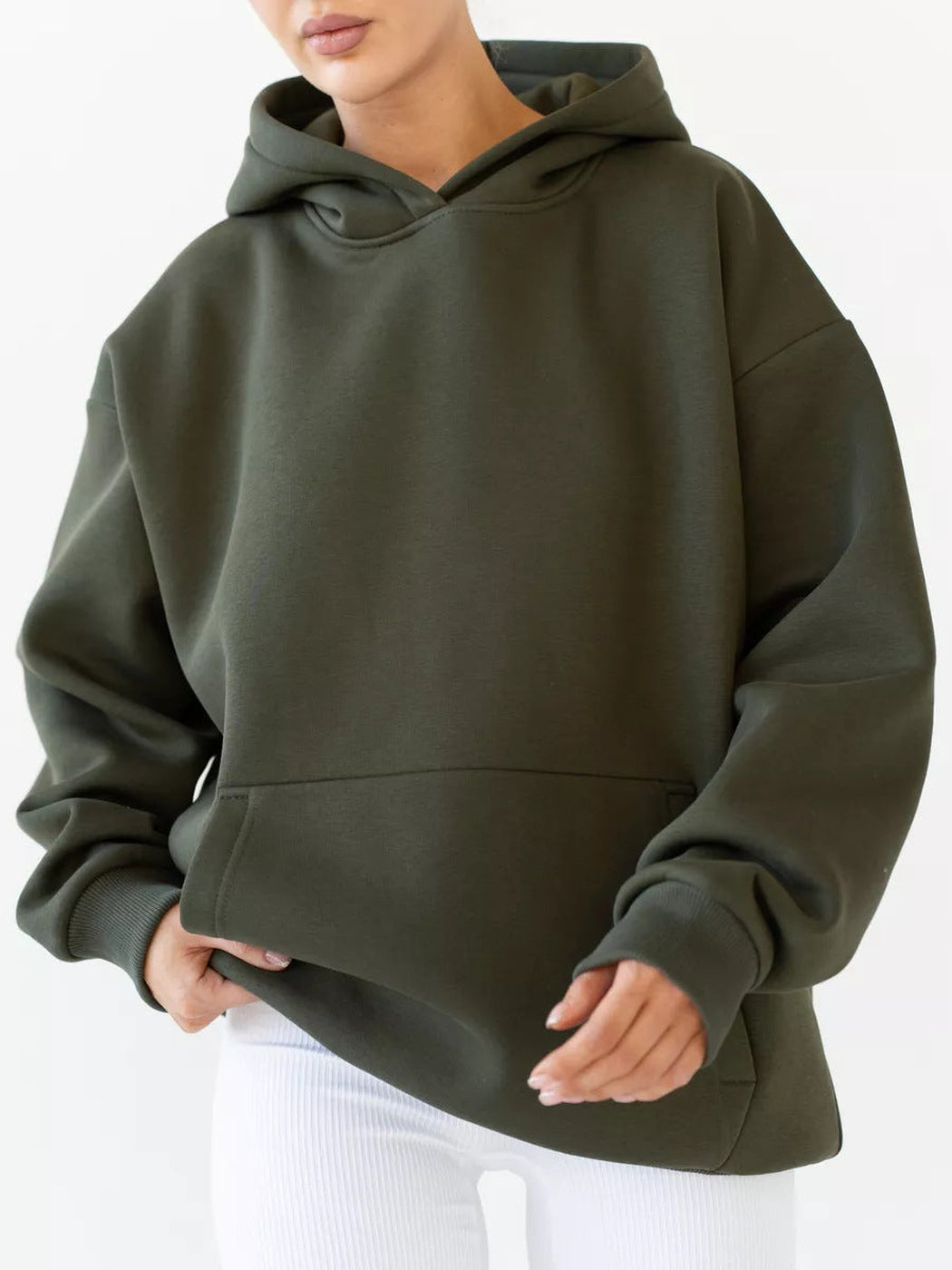 Vrouw in een olijfgroene hoodie met een witte legging, hand bij de zoom | Boutique Moda