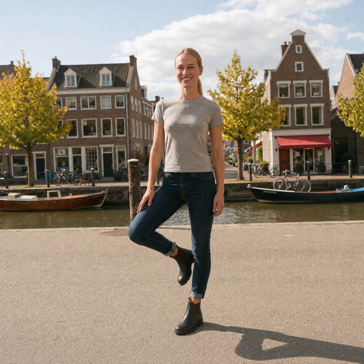 A person's lower legs in dark jeans wearing dark olive green Chelsea boots with brown elastic side panels and tan pull tabs, standing on a plain grey background, lifestyle view