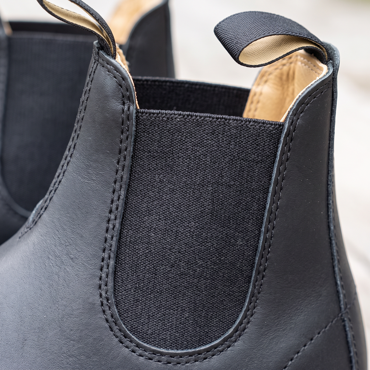 A black leather Chelsea-style ankle boot with elastic side panels and fabric pull tabs, shown on a plain light background, close-up view