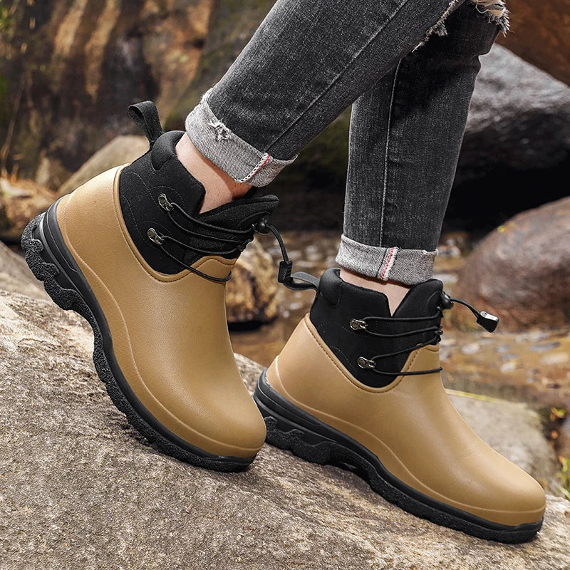 Kaki regenlaarzen met zwarte details, gedragen door een persoon buiten op rotsen | Boutique Moda