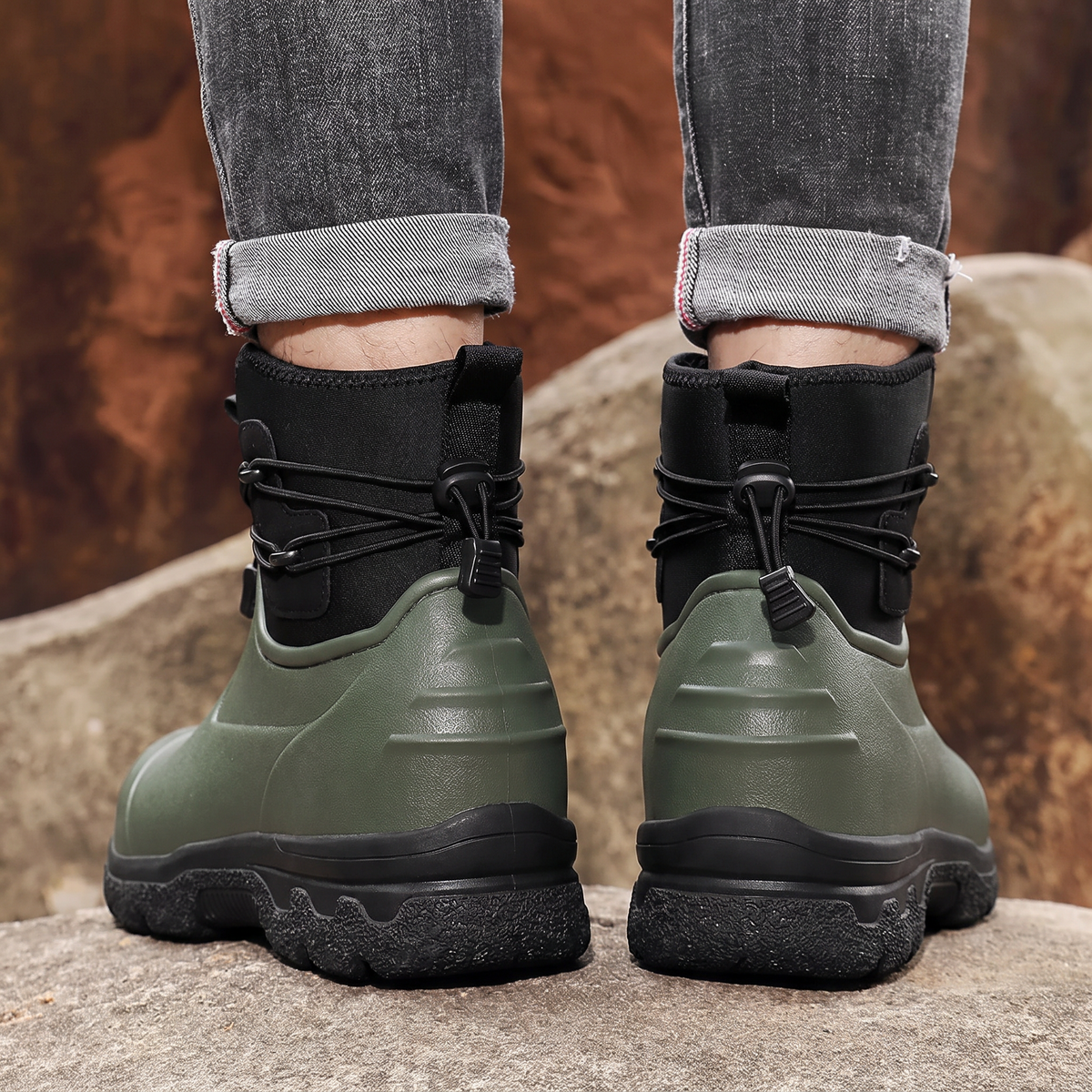 Groene en zwarte regenlaarzen met veters, gedragen door een persoon op rotsen | Boutique Moda