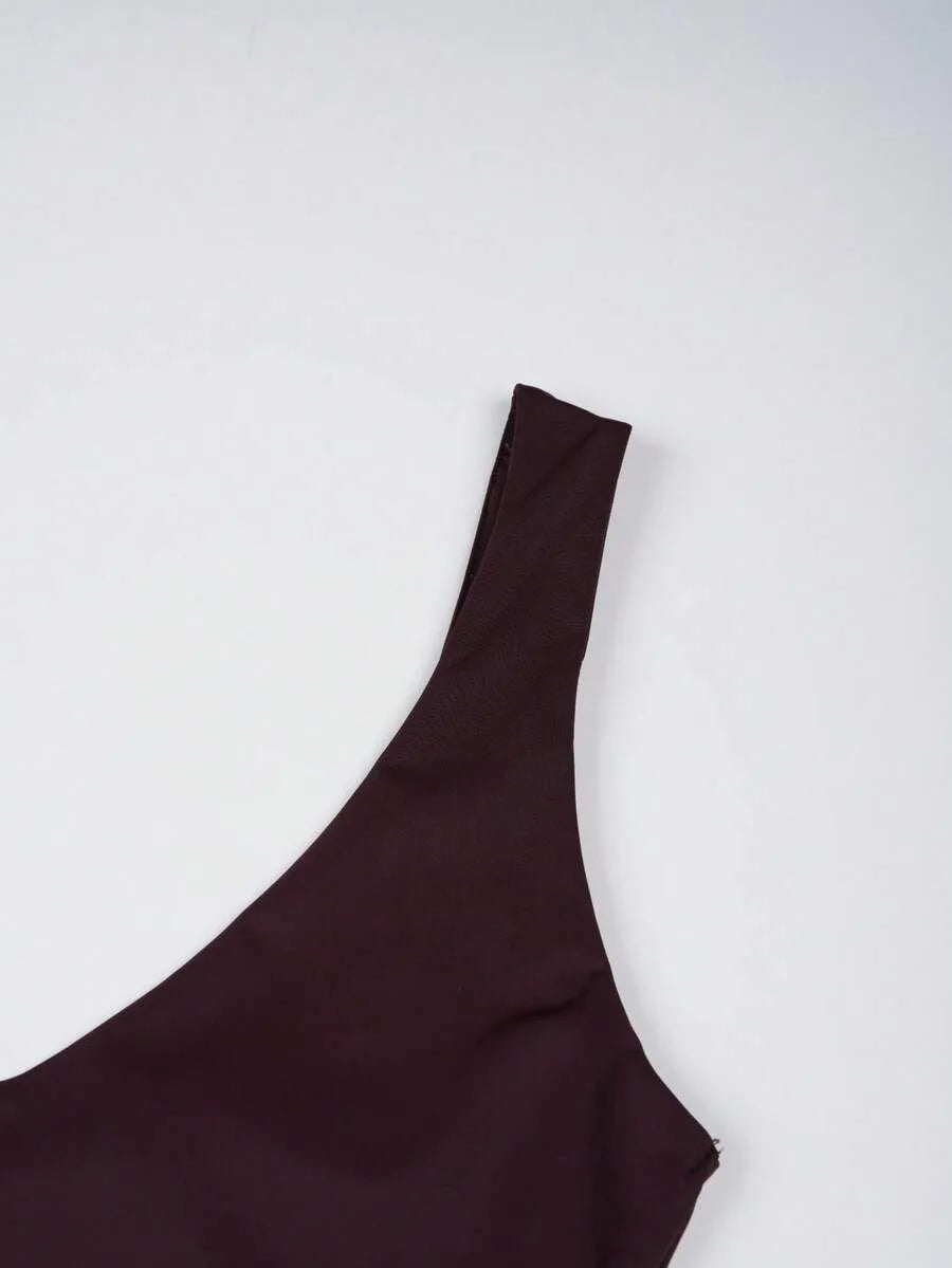Close up of a dark maroon bodysuit shoulder strap and neckline against a plain background.