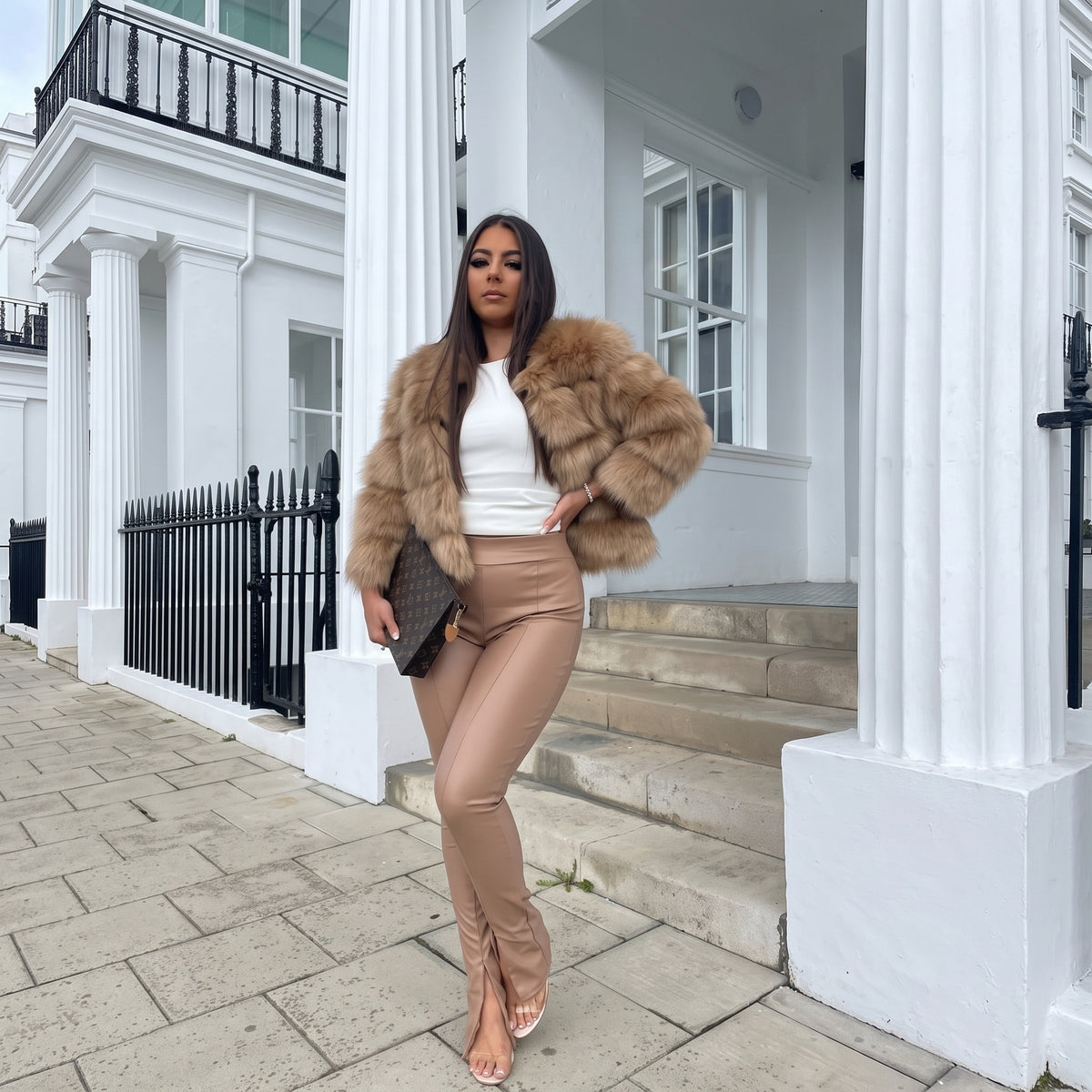 Vrouw draagt kort beige fluffy jasje met witte top en beige broek | Boutique Moda