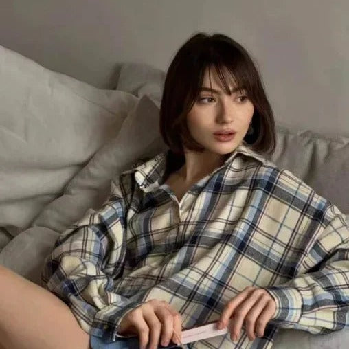 Vrouw draagt geruite oversized blouse in beige en marineblauw, zittend op bank | Boutique Moda