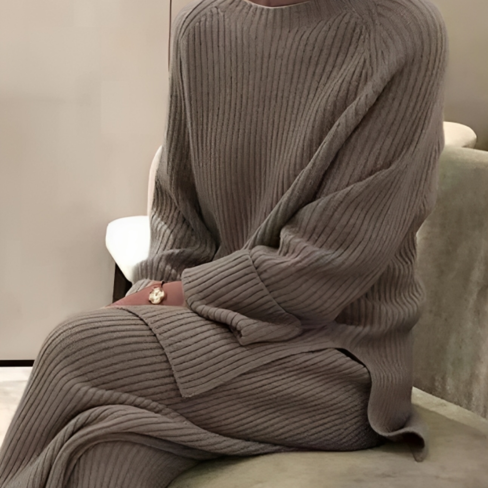 Grijze geribbelde tweedelige loungeset, gedragen door zittende vrouw met tas | Boutique Moda