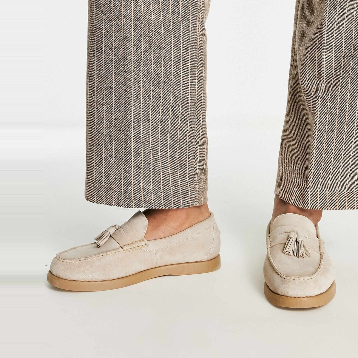 Beige suède loafers met kwastjes gedragen door persoon in gestreepte broek | Boutique Moda