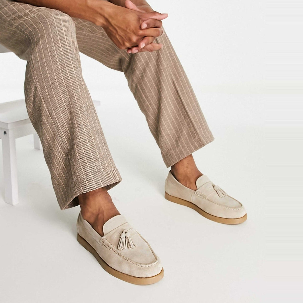 Beige suède loafers met kwastjes, gedragen door persoon op witte kruk | Boutique Moda