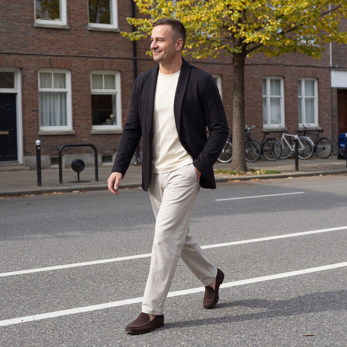 Man draagt een zwarte herenblazer met sjaalkraag en open voorkant over een crème T-shirt, lopend in een straat in Utrecht | Boutique Moda