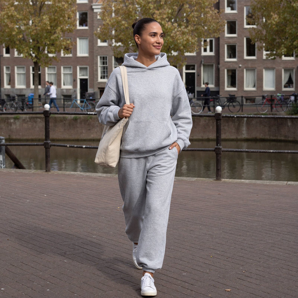 Vrouw draagt grijs trainingspak met oversized hoodie en joggingbroek langs een gracht in Amsterdam | Boutique Moda