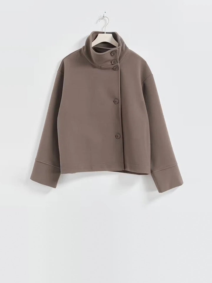 Taupe kortjas met opstaande kraag en knopen, hangend op hanger | Boutique Moda