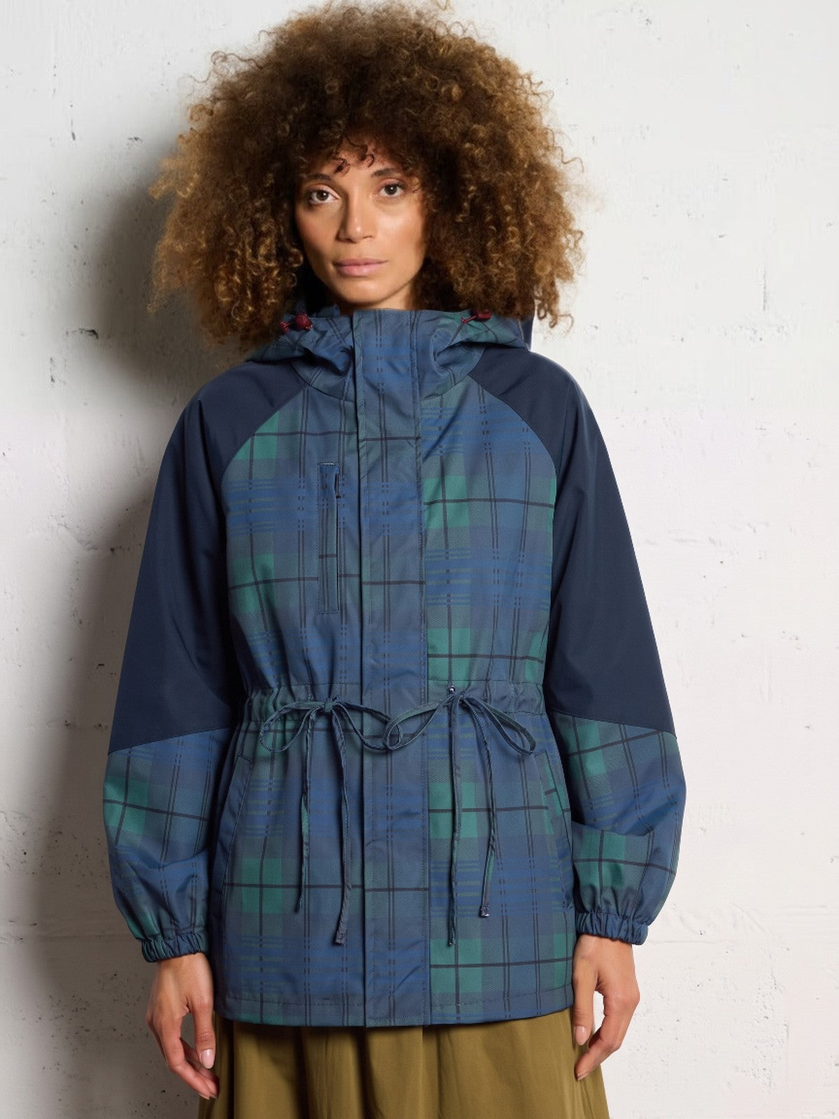 Vrouw in een geruite blauwgroene regenjas met geruite capuchon, rechte mouwen en taillekoord | Boutique Moda