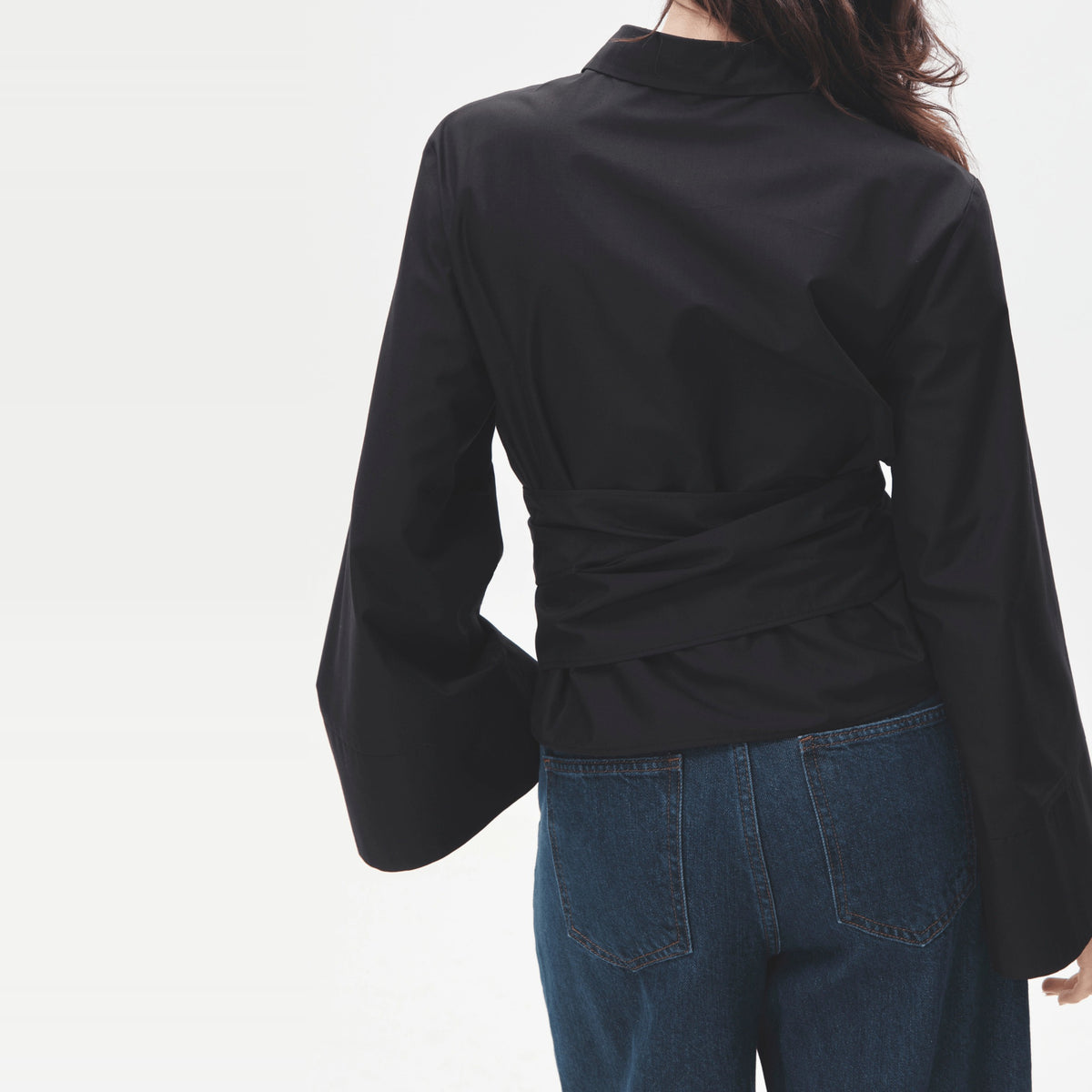 Vrouw draagt donkere wikkelblouse met wijde mouwen, gekruiste ceintuur op de rug, achteraanzicht | Boutique Moda