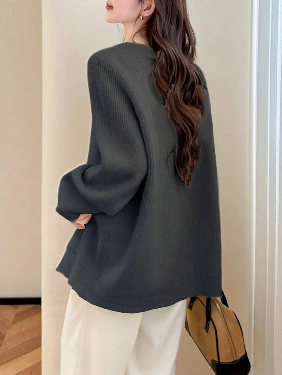 A woman seen from behind wearing an oversized dark grey ribbed knit cardigan with white wide leg pants, carrying a tan and black handbag.