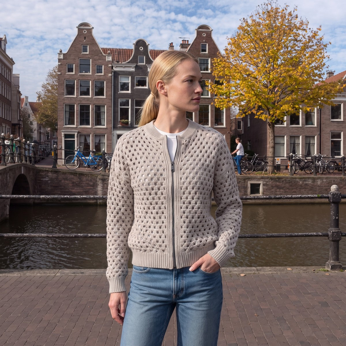Vrouw in een lichtgrijs opengewerkt vest met rits aan een Amsterdamse gracht